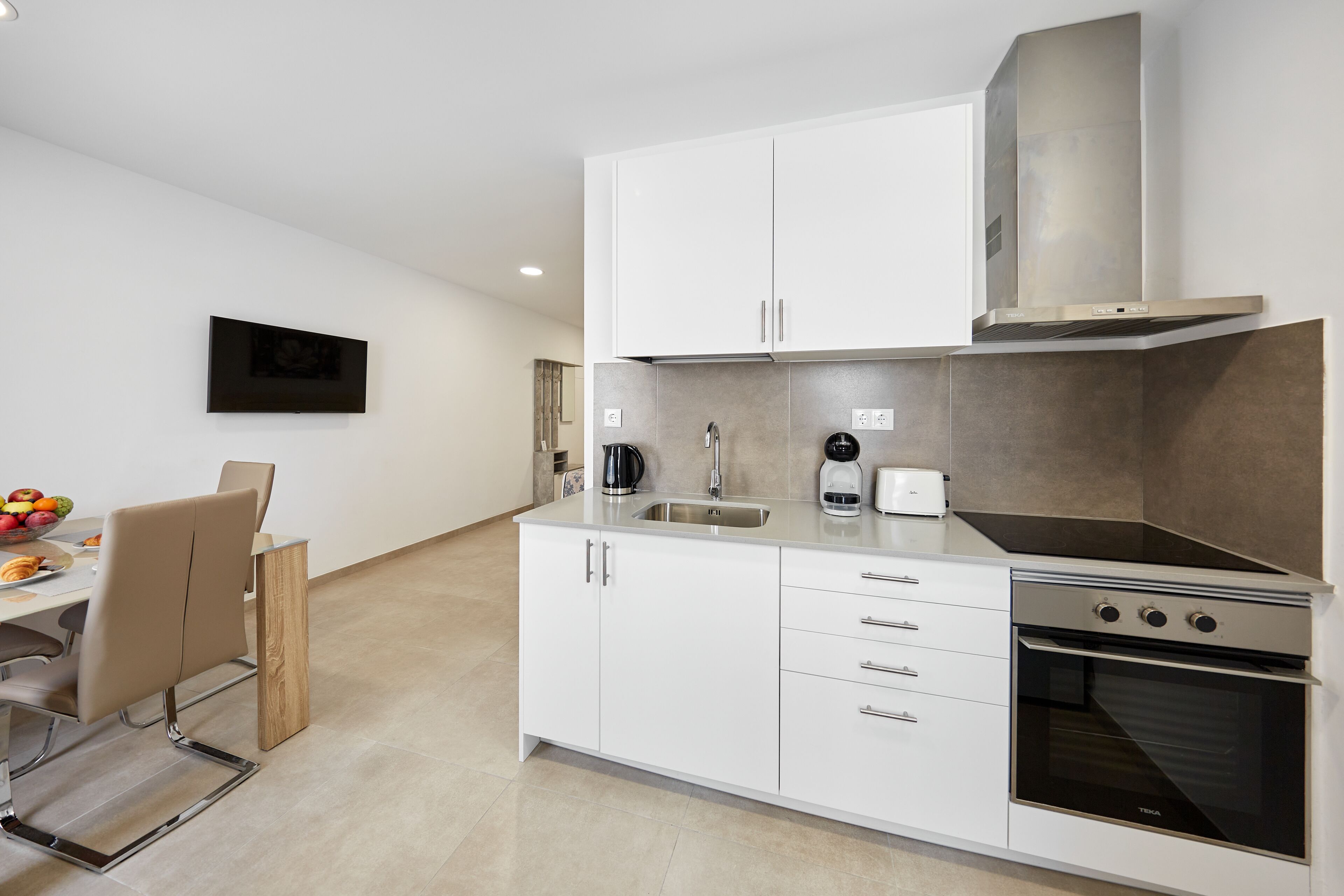 A modern kitchen with white cabinetry, a stainless steel range hood, and a built-in oven.
