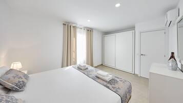 A modern hotel room with a large bed, a bedside table with a lamp, a wardrobe, and a mirror.