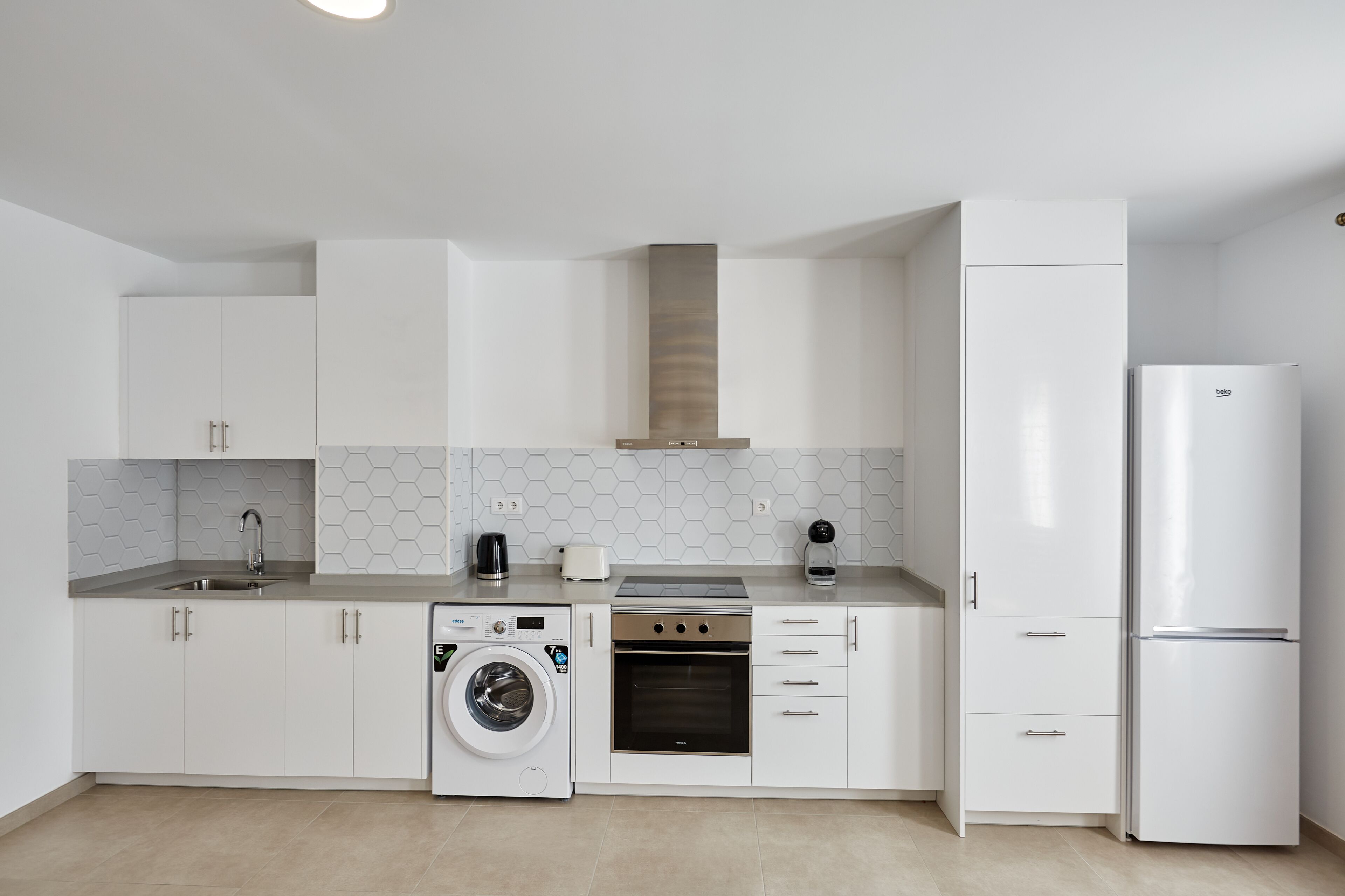 Una cocina moderna con muebles blancos, lavadora integrada, estufa y refrigerador.