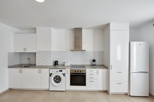 Una cocina moderna con muebles blancos, lavadora integrada, estufa y refrigerador.