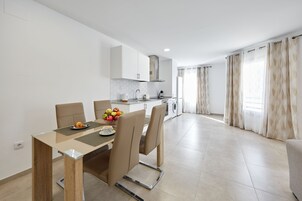 A modern kitchen with white cabinets, a built-in oven, and a dining area with a table and chairs.