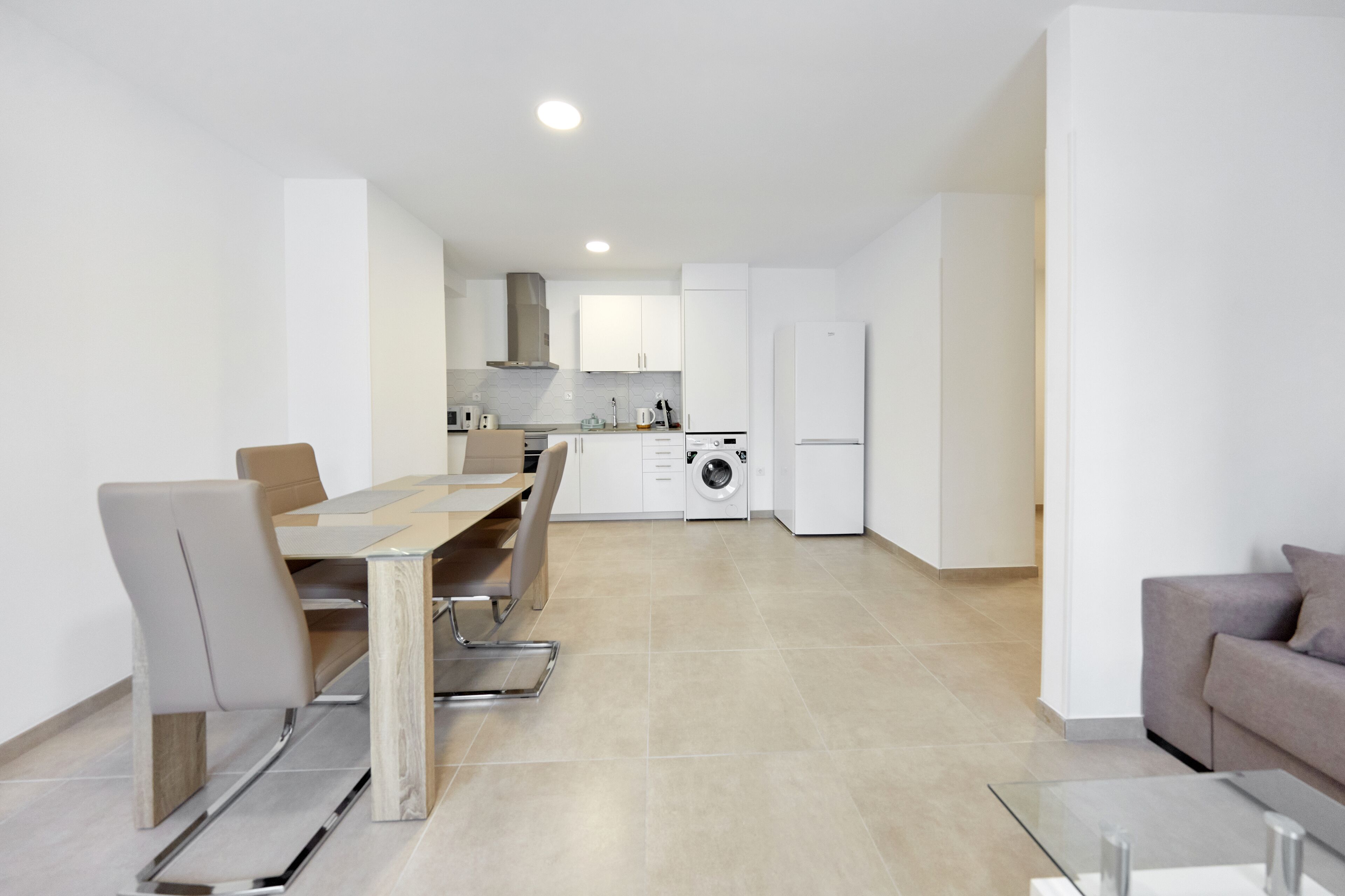 Una cocina moderna con armarios blancos, un comedor con mesa y sillas, y una lavadora integrada.