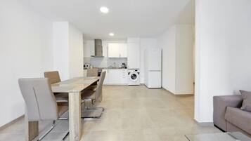 Una cocina moderna con armarios blancos, un comedor con mesa y sillas, y una lavadora integrada.