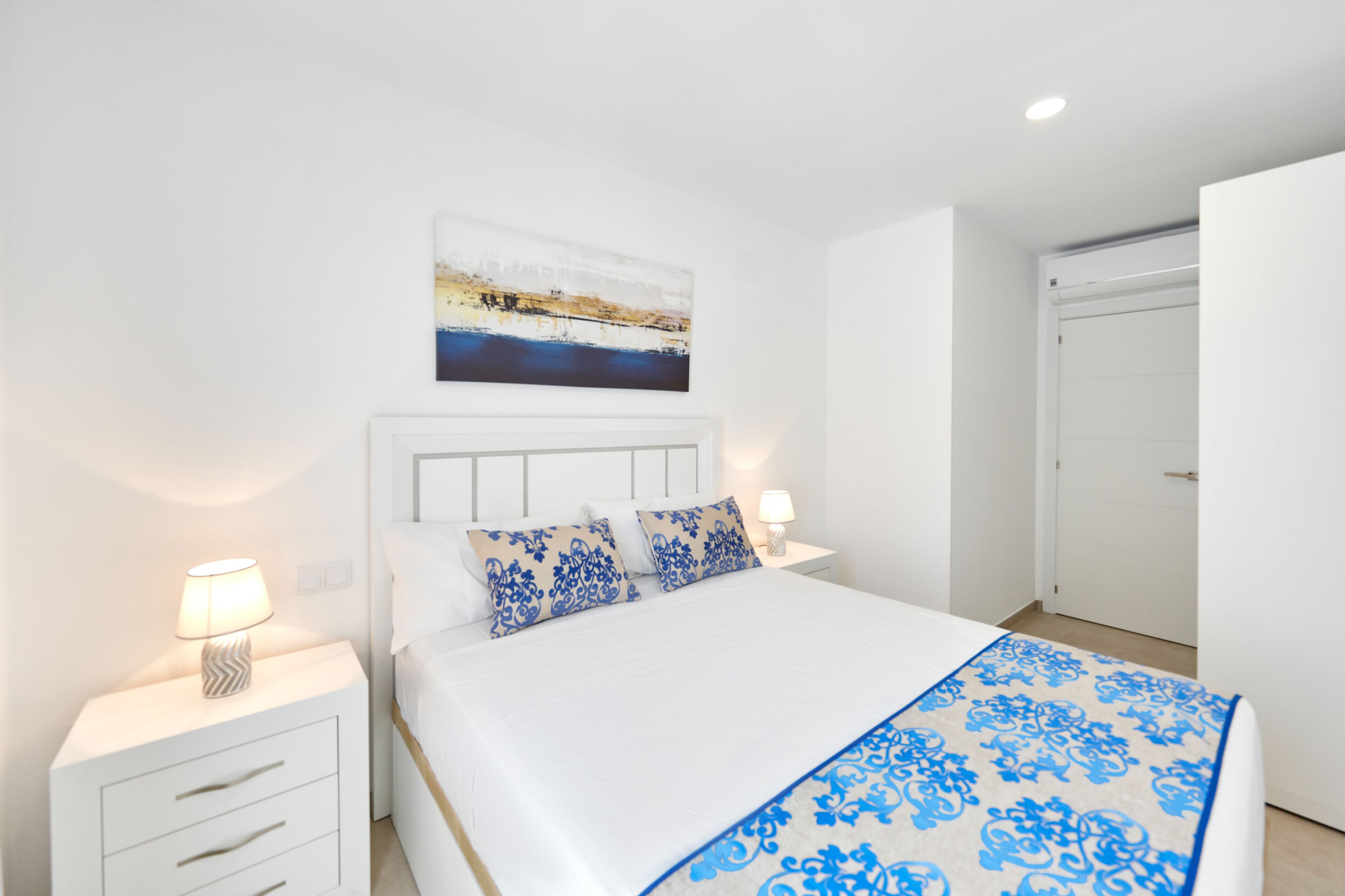 Une chambre à coucher avec un lit, des tables de chevet, un tableau et une porte.
