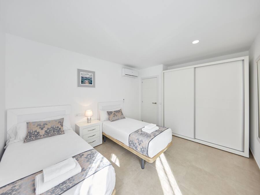Habitación de hotel con dos camas individuales, una mesita de noche con lámpara, un armario y un equipo de aire acondicionado.