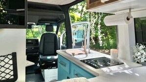 Een compact RV-interieur met een kitchenette, een zithoek en een televisie waarop 'The Roku Channel' wordt weergegeven.