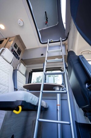 A compact RV interior with a ladder, a small table, and a window.