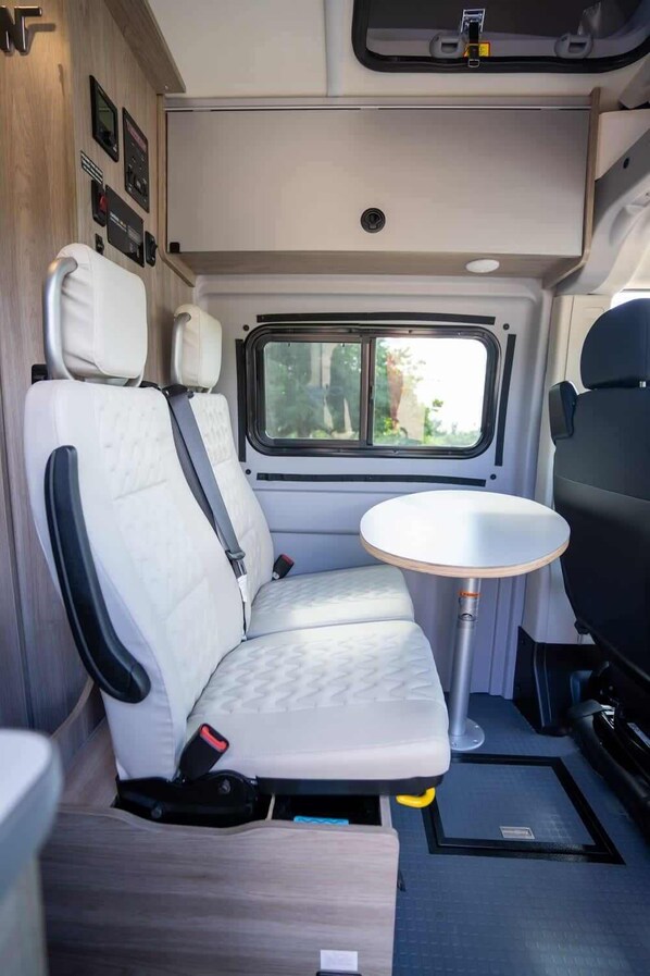 A compact RV interior with a single seating area, a small table, and a window providing a view of the outdoors.