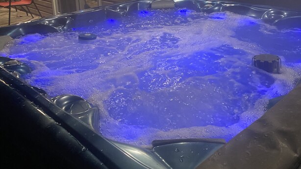 Een bubbelbad met blauwe verlichting, omringd door een houten terras en een glazen deur.