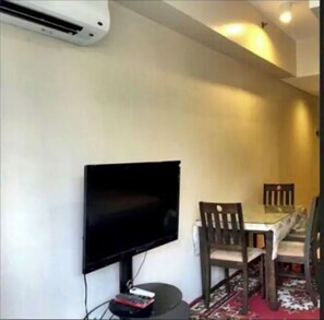 A small dining area with a TV mounted on the wall, a table, and two chairs.