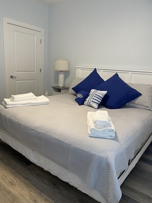 Un lit bien fait, avec du linge de lit blanc et des oreillers bleus, une lampe de chevet et une porte, dans une chambre d’hôtel.