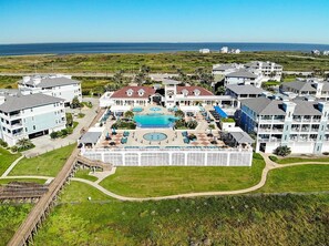 An aerial view of a resort with a central pool, multiple buildings, and a beach in the background. - Beach Front and steps away from Pointe West Community amenities! (Galveston)