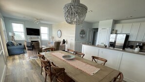 Un grand espace à manger avec une table en bois, entourée de chaises en bois, dans une cuisine moderne dotée de meubles blancs et d’appareils électroménagers en acier inoxydable.