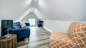 A modern loft bedroom with a sloped ceiling, a blue sofa, a patterned orange couch, and a wooden side table. - Stylish Condo Close To Everything!  (Indianapolis)