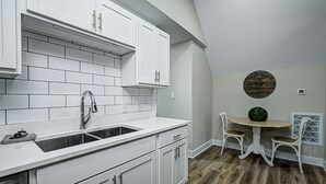 A kitchen with white cabinets, a sink, and a dining area with a round table and chairs. - Stylish Condo Close To Everything!  (Indianapolis)