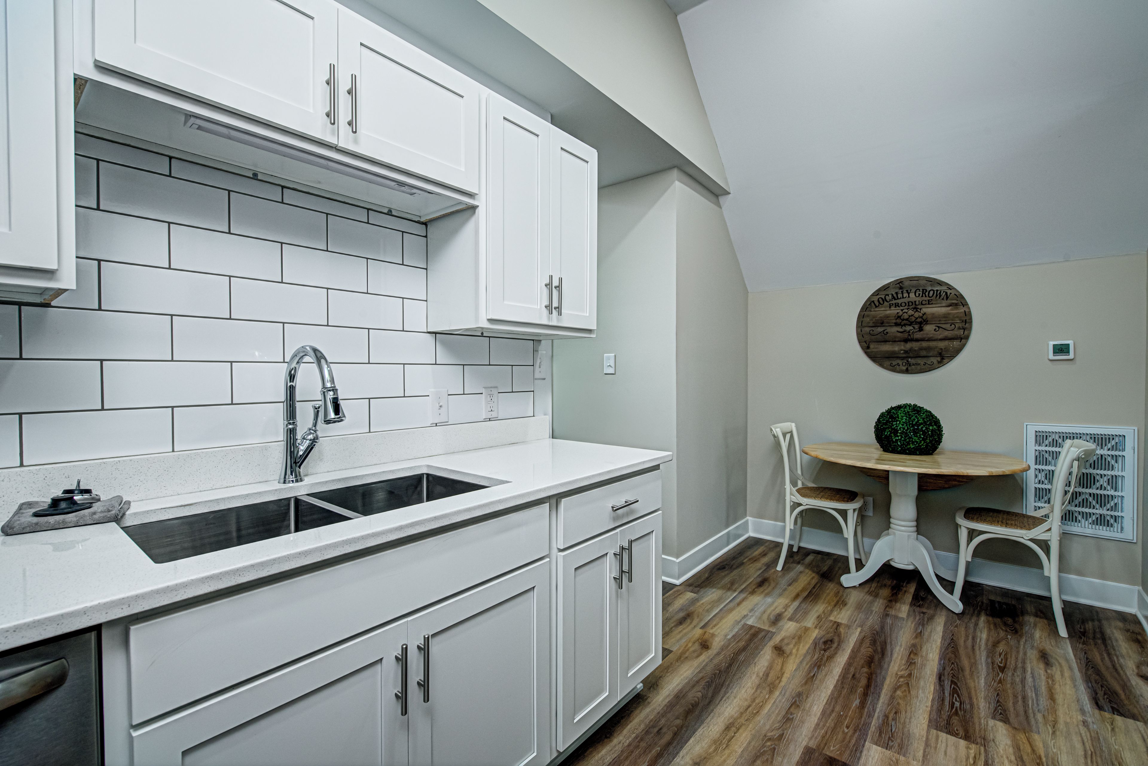 A kitchen with white cabinets, a sink, and a dining area with a round table and chairs.