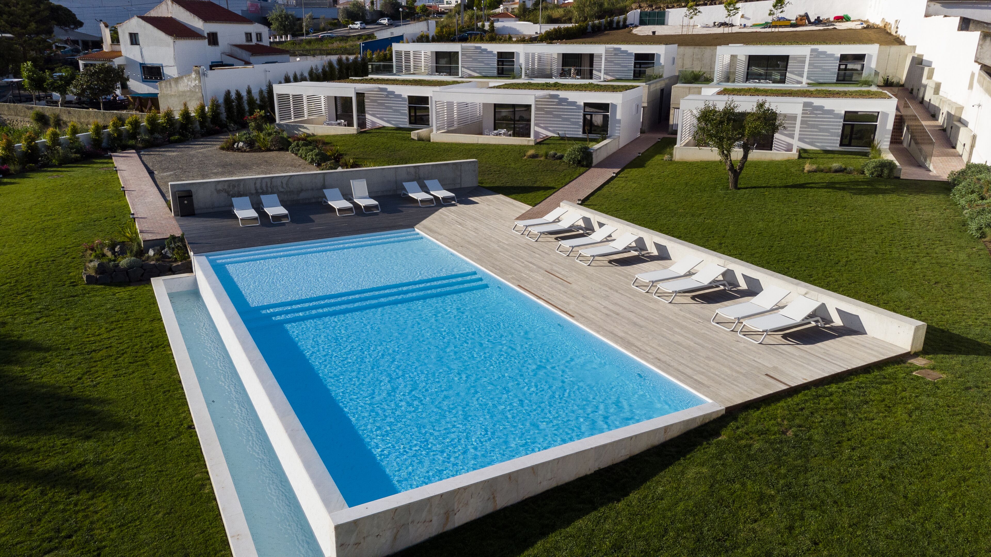Un espace piscine moderne doté d’une longue piscine rectangulaire, de plusieurs chaises longues et d’une pelouse bien entretenue.