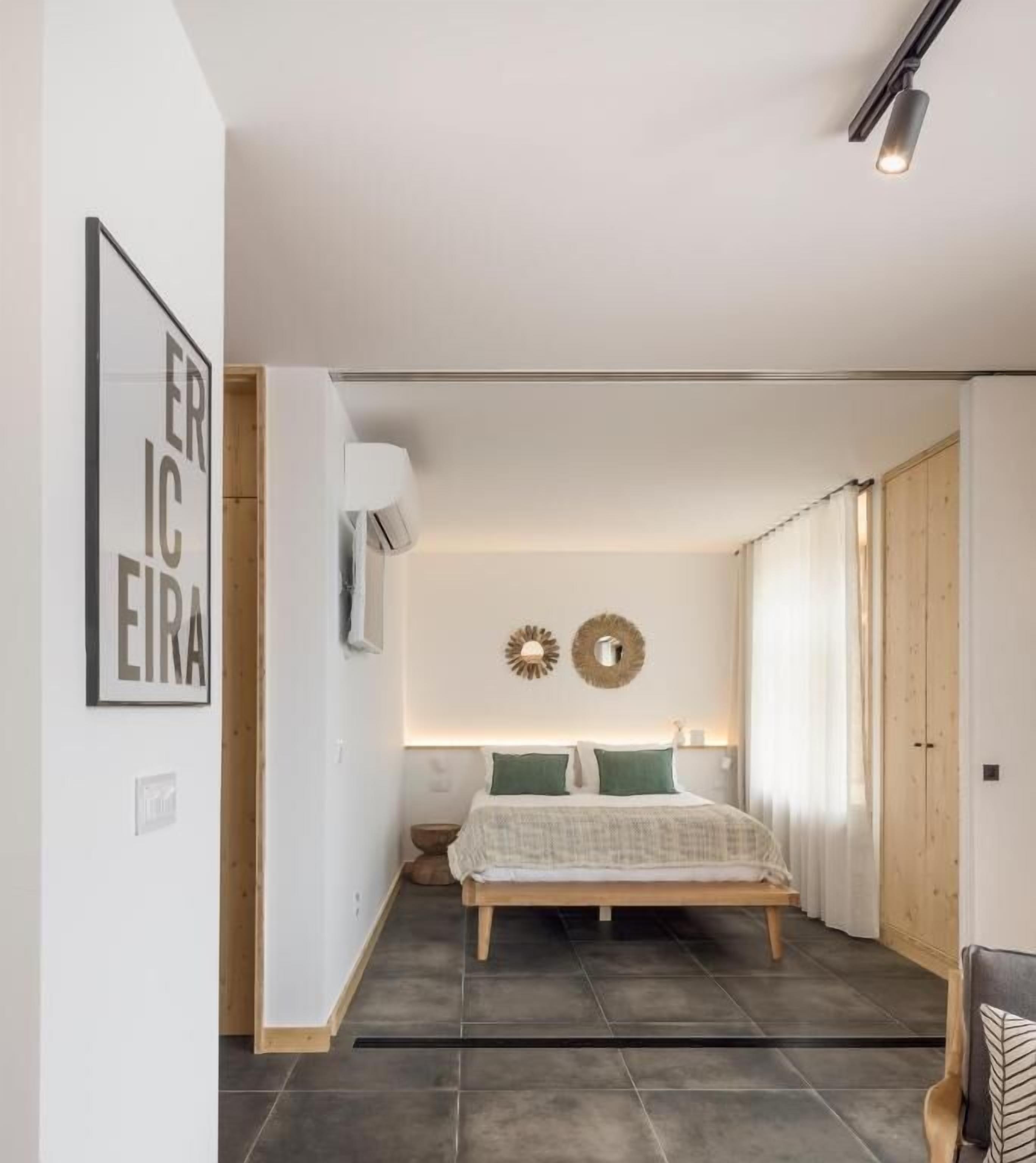 A bedroom with a bed, a wall-mounted air conditioner, a framed picture, and a wooden door.