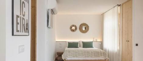 A bedroom with a bed, a wall-mounted air conditioner, a framed picture, and a wooden door.