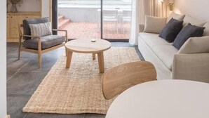 Een moderne woonkamer met een grote schuifpui naar een terras, een bank, een fauteuil, een ronde houten salontafel en een geweven vloerkleed.