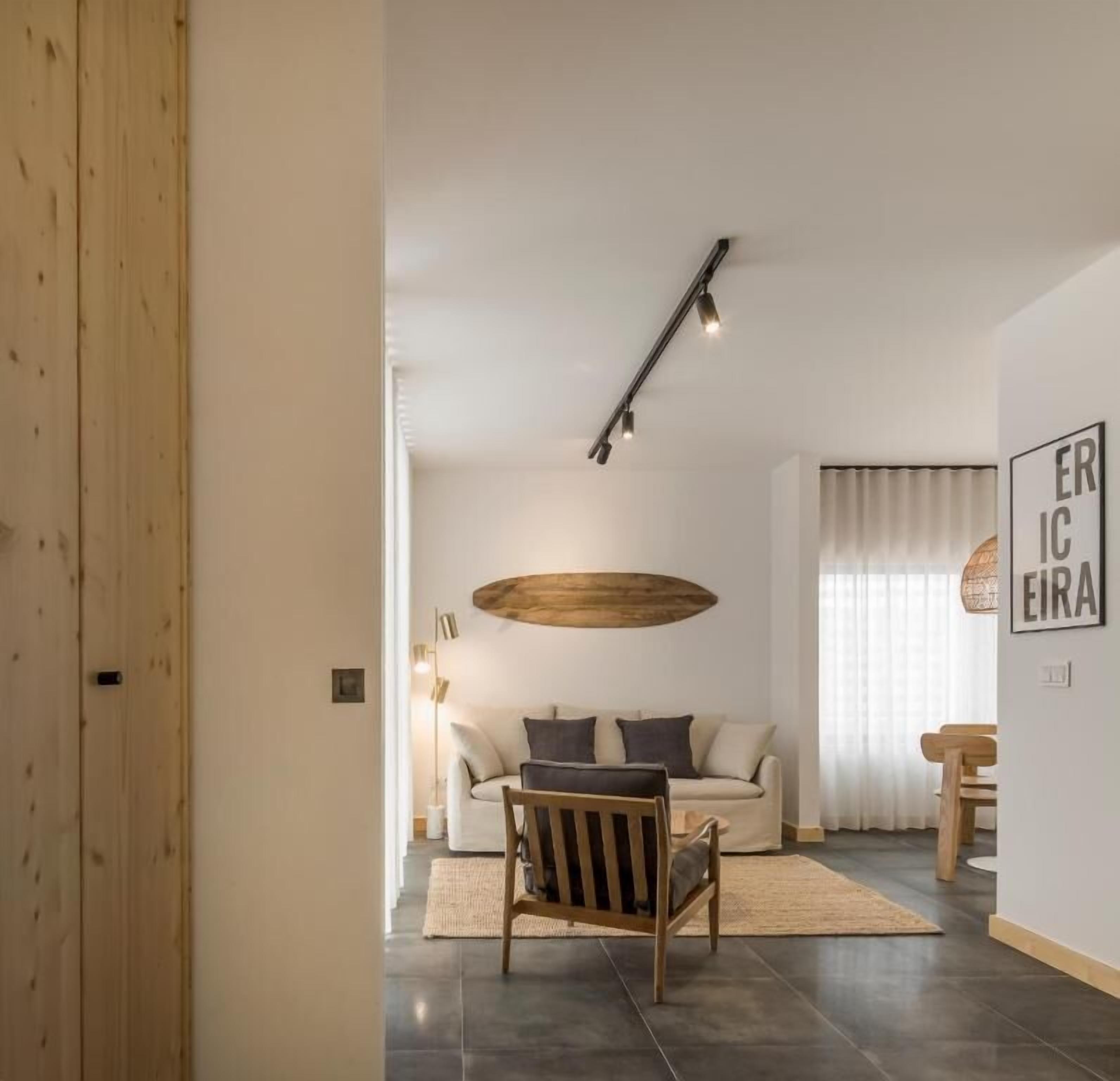 Un salon moderne avec un canapé, une chaise en bois, un luminaire suspendu et un tapis.