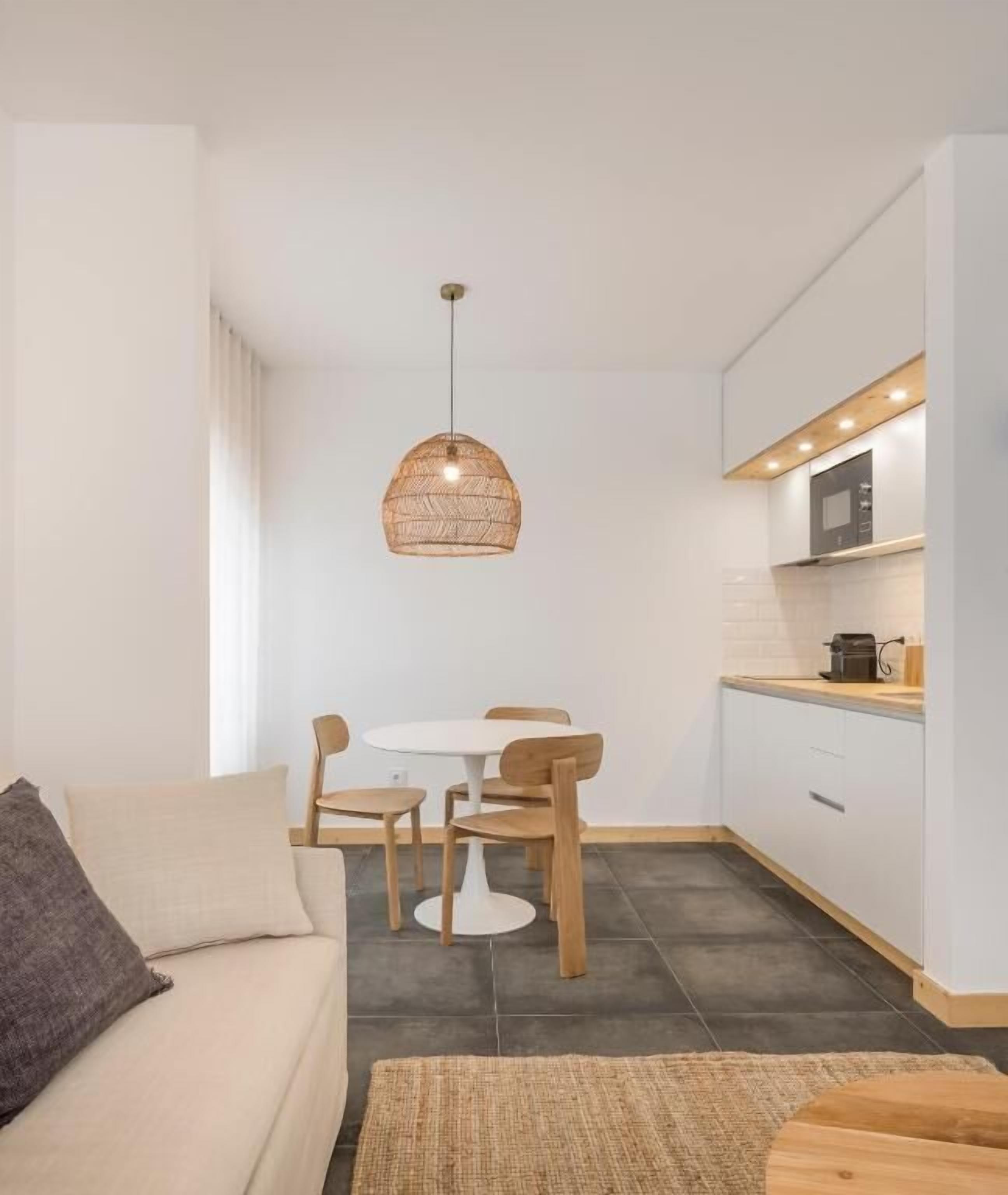 A compact living space with a kitchenette, a dining area with a round table and chairs, and a sofa with a throw pillow.