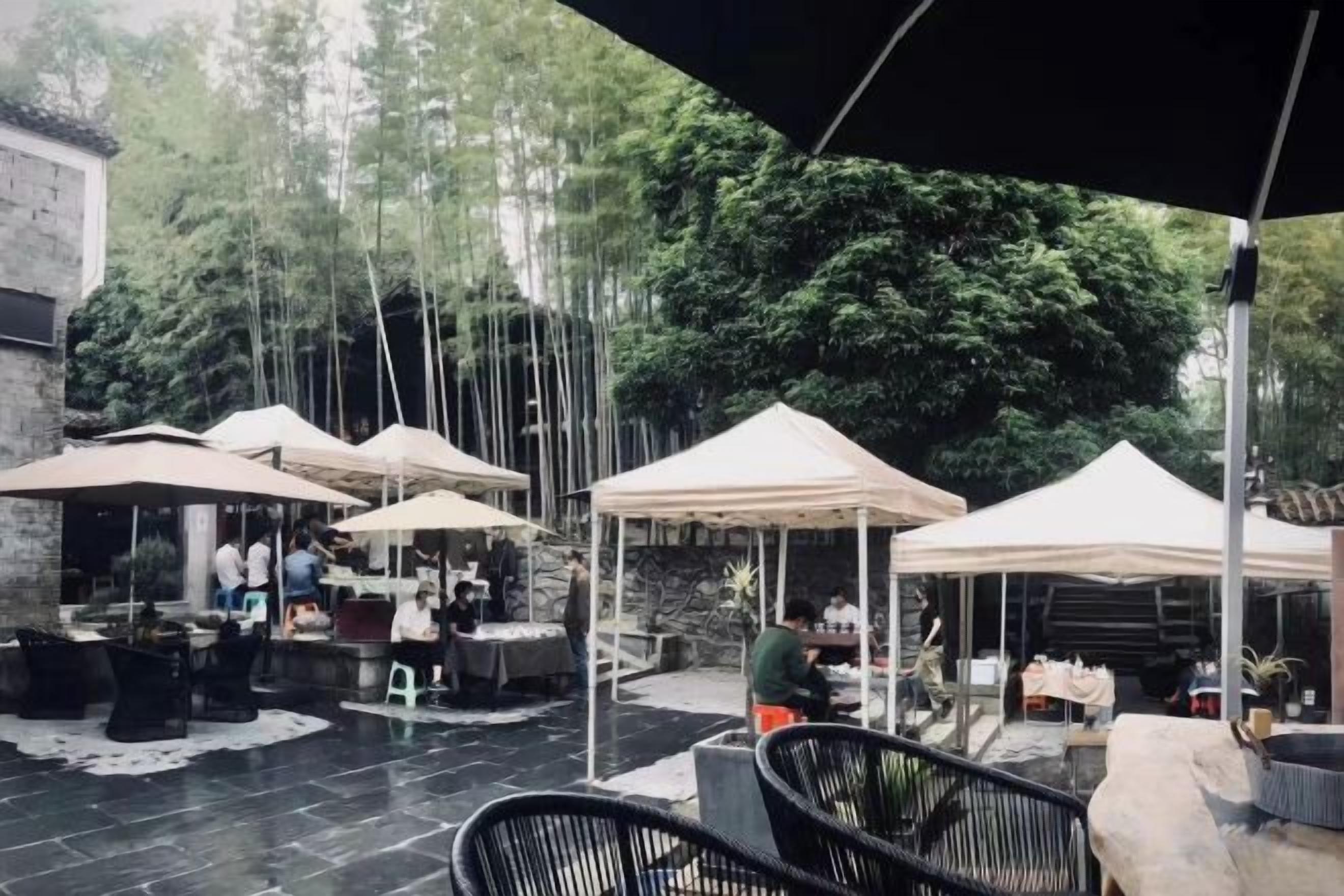 An outdoor patio area with tables and chairs under umbrellas, surrounded by trees.