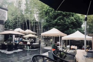 An outdoor patio area with tables and chairs under umbrellas, surrounded by trees. - Jingdezhen Guiran Inn (Jingdezhen)