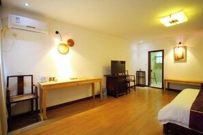 A hotel room with a wooden floor, a bed, a desk, a chair, a television, and a wall-mounted air conditioner.