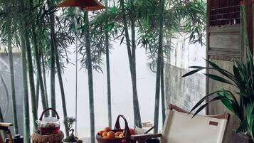 Un comedor con una mesa preparada para dos personas, una lámpara colgante y vista a bambúes.