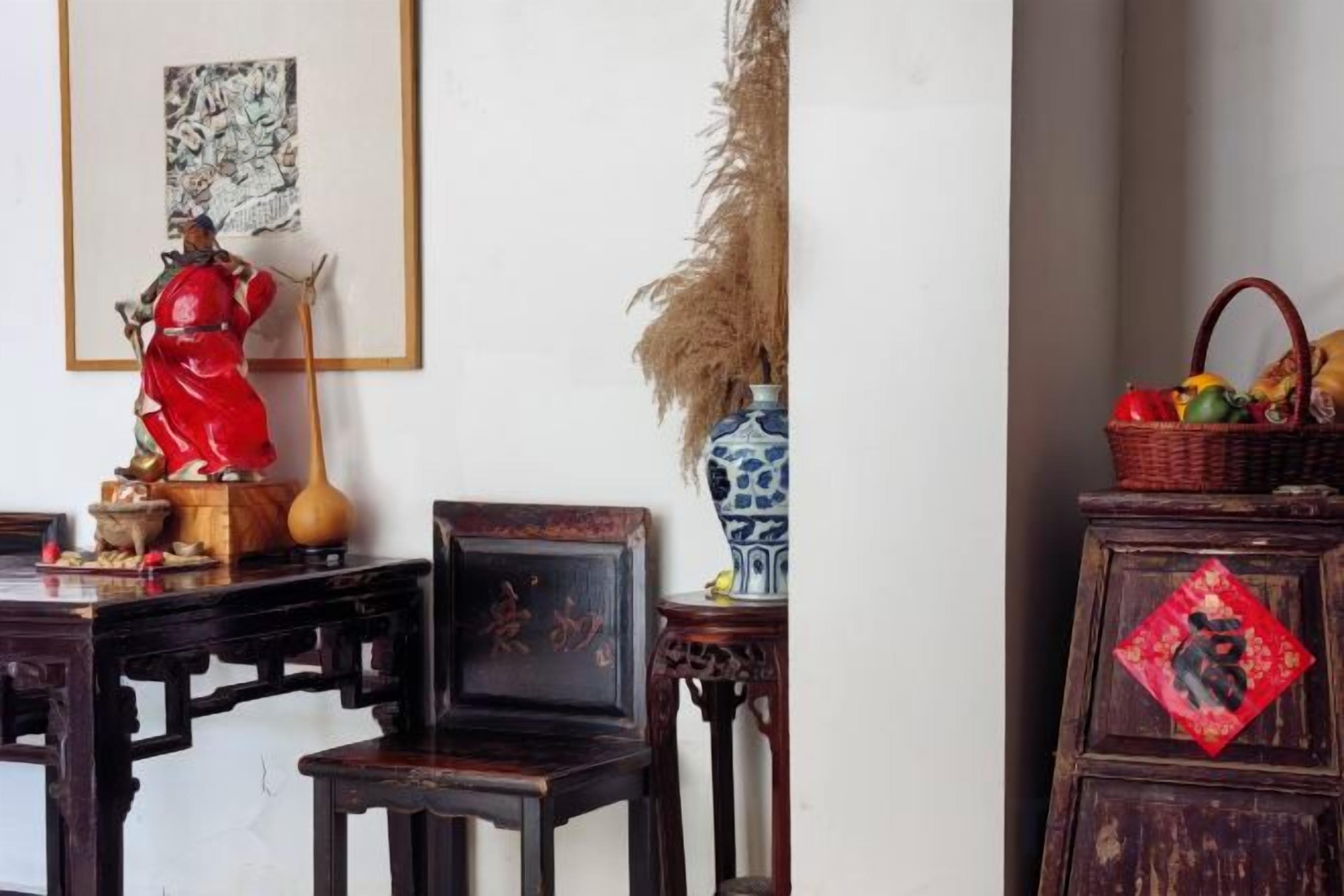 Quarto tradicional com mesa de madeira, cadeiras, uma estátua, um vaso e um armário com painel decorativo vermelho.