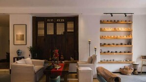 A living room with a sofa, a coffee table, a wooden cabinet with shelves, and a traditional door. - Jingdezhen Guiran Inn (Jingdezhen)