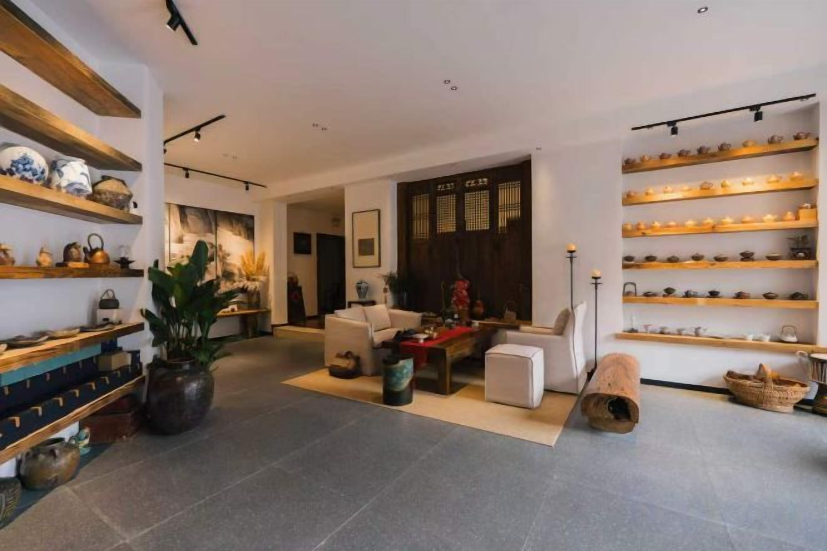 A modern living room with a sofa, coffee table, and decorative items. There are shelves with various objects on the walls.