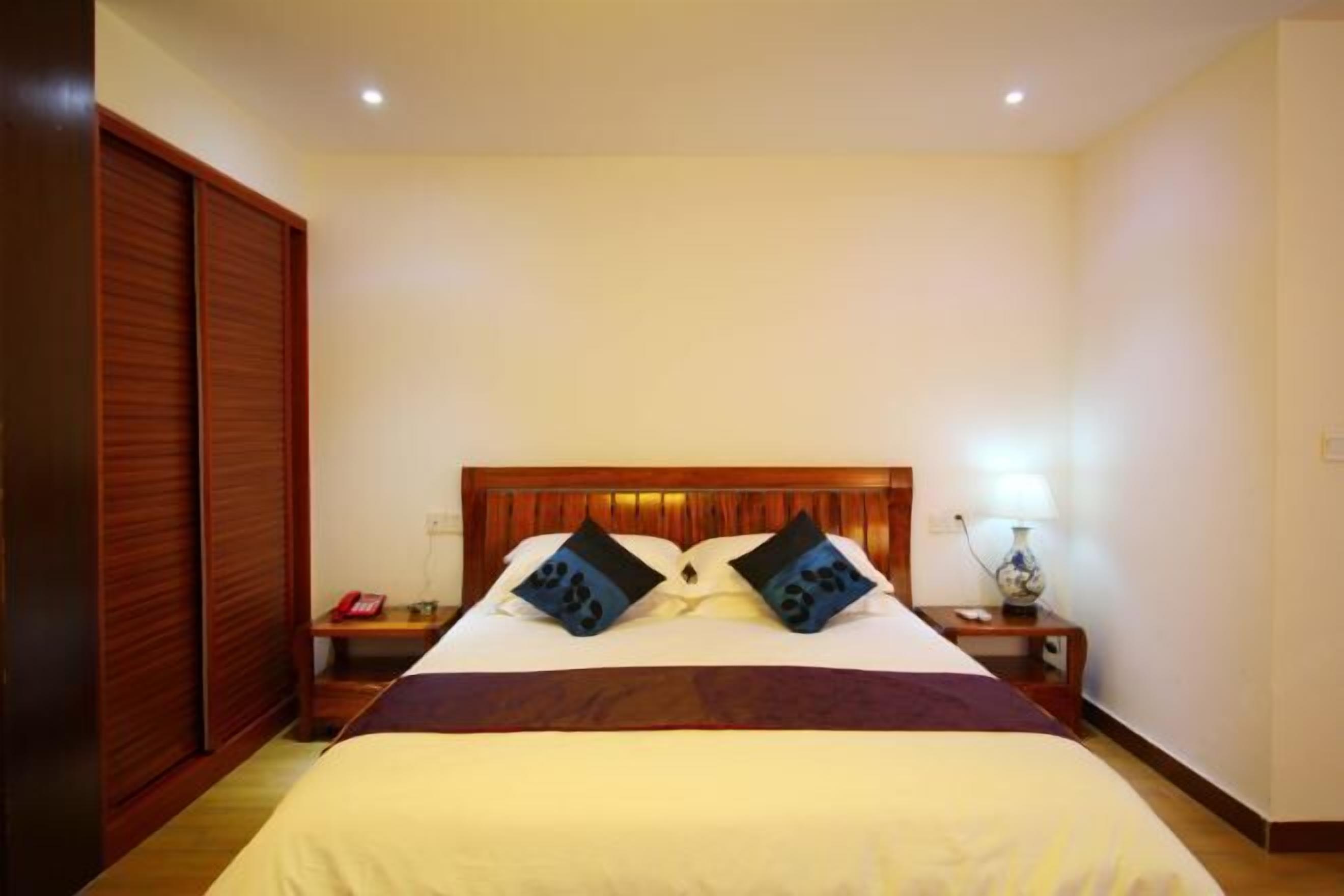 Quarto de hotel com uma cama grande, cabeceira de madeira, duas mesas de cabeceira com abajures e um guarda-roupa.