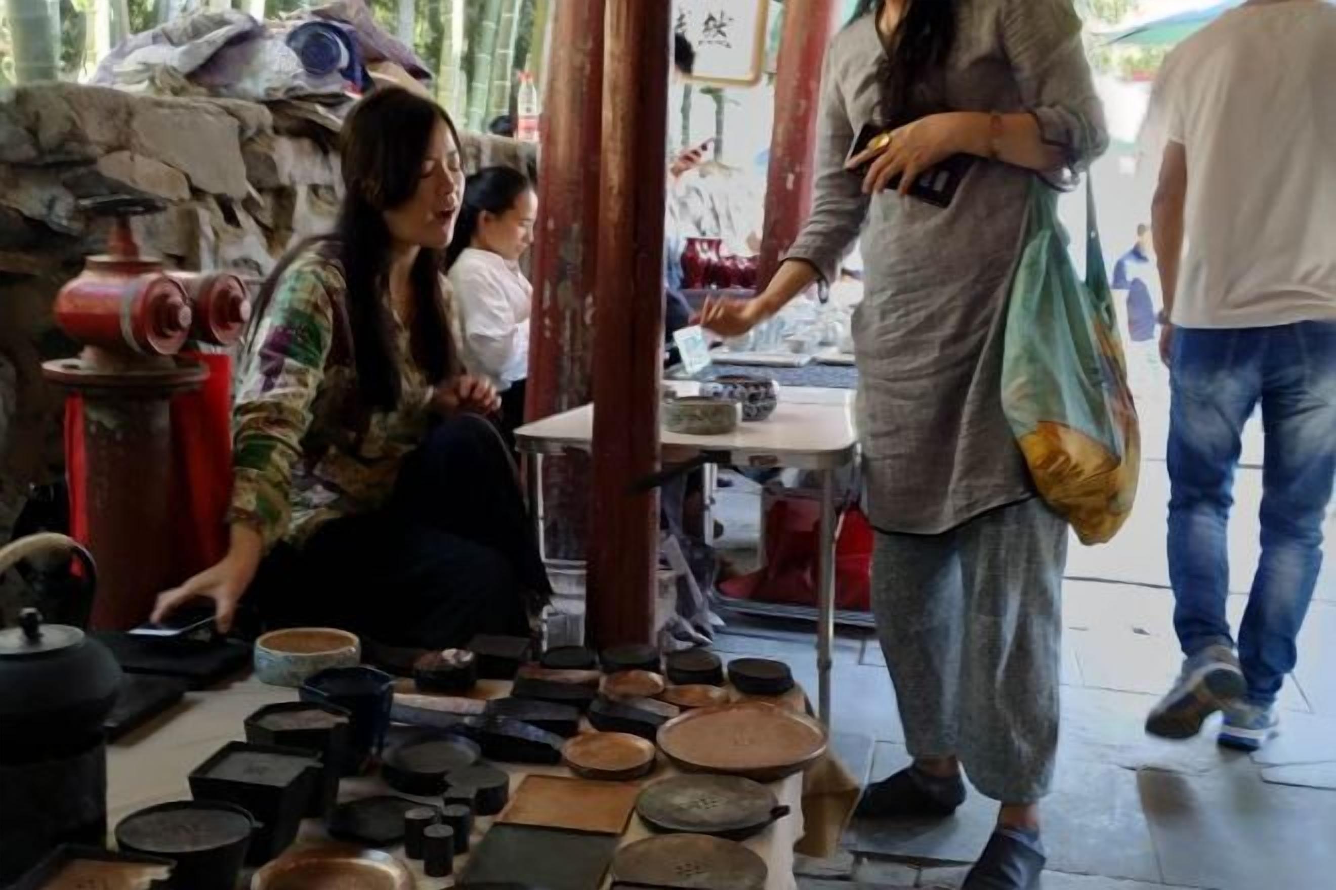 A person seated on the floor surrounded by various pottery items.