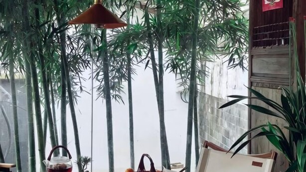 A table with a teapot, cups, and a basket of oranges, surrounded by bamboo plants and a hanging lamp. - Jingdezhen Guiran Inn (Jingdezhen)