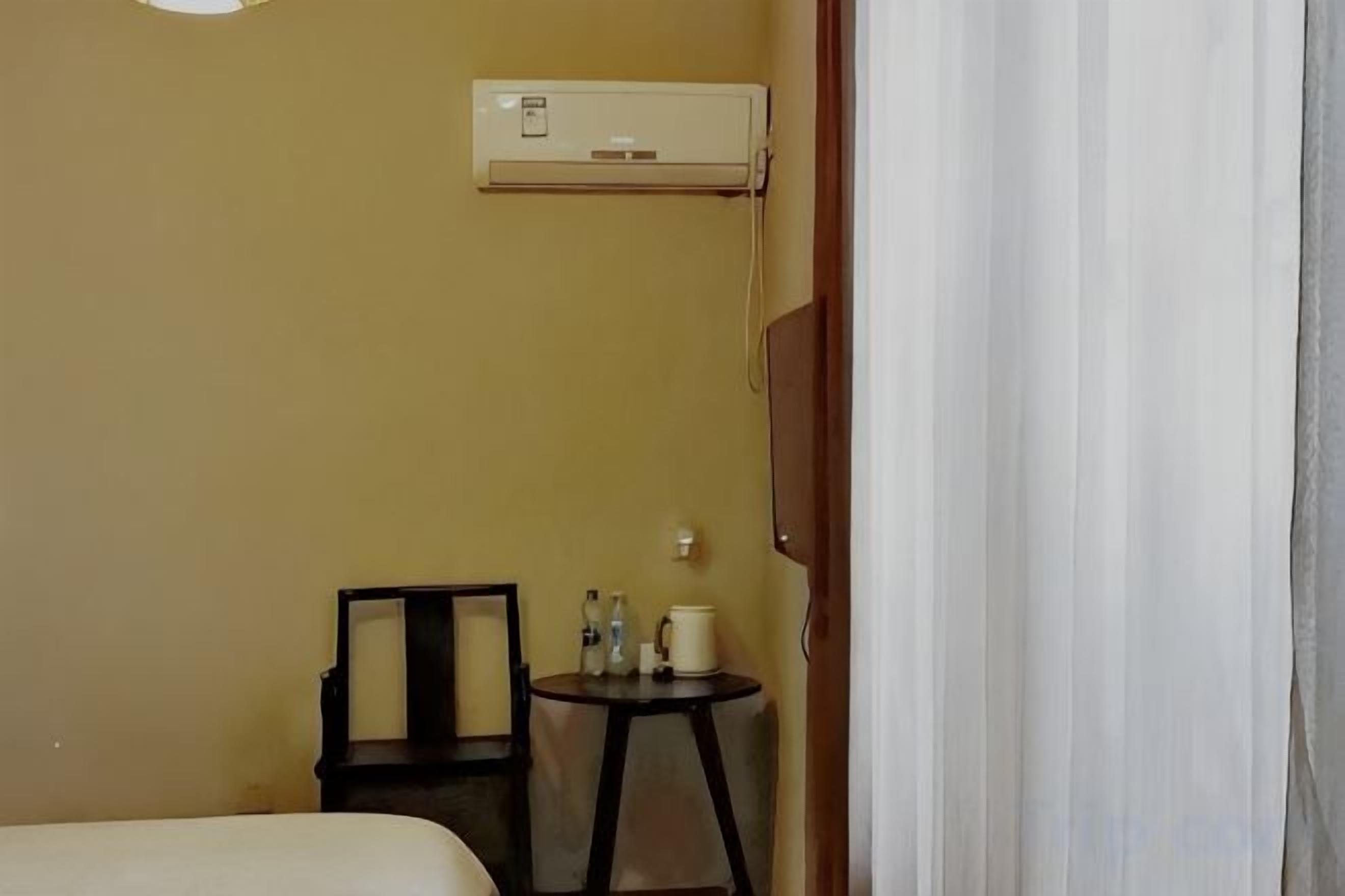 Habitación de hotel con una cama, una pequeña mesa con una silla, un equipo de aire acondicionado en la pared y una cortina entreabierta.