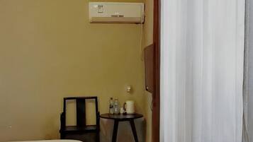Habitación de hotel con una cama, una pequeña mesa con una silla, un equipo de aire acondicionado en la pared y una cortina entreabierta.
