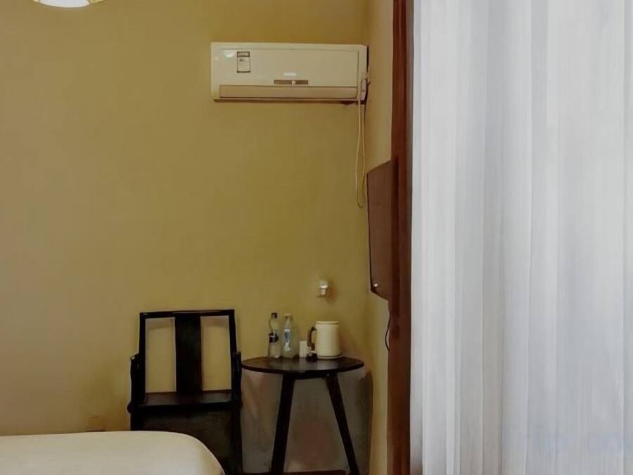 Habitación de hotel con una cama, una pequeña mesa con una silla, un equipo de aire acondicionado en la pared y una cortina entreabierta.