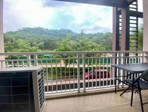 A balcony with a view of a green landscape and a red car on the street.