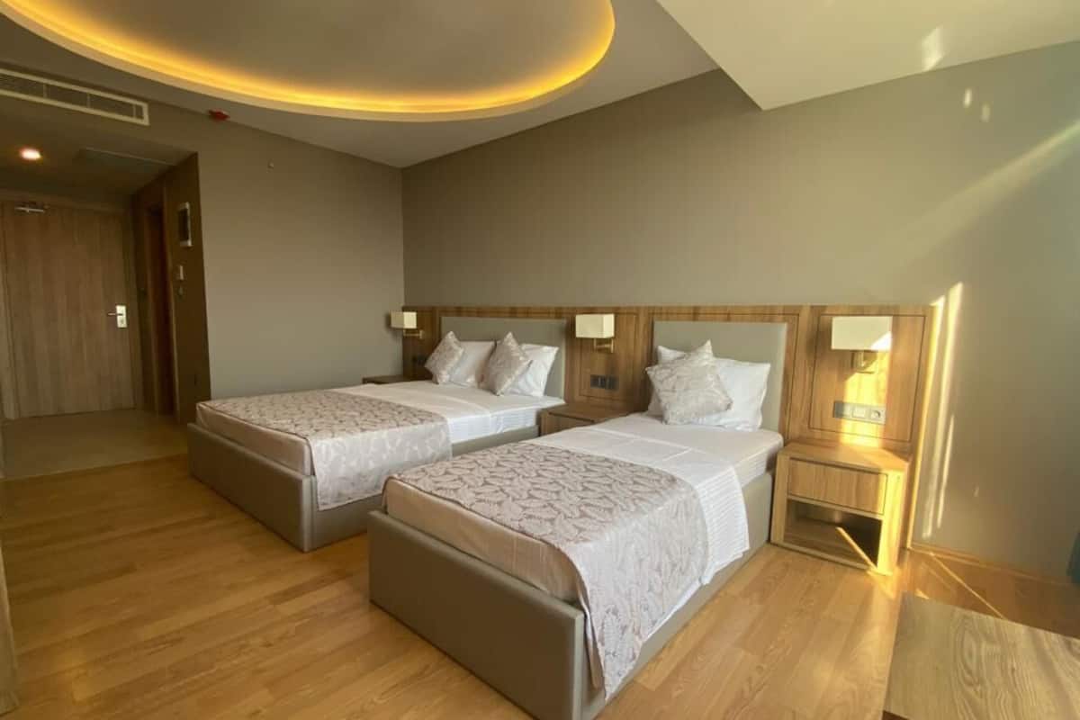 Habitación de hotel con dos camas, piso de madera y un diseño moderno en el techo.