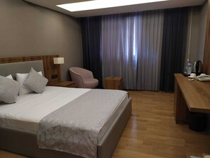 A hotel room with a large bed, a desk, a chair, a nightstand, and a window with curtains. - KARTAL PARK OTEL (Sirnak)