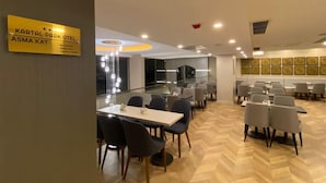 A modern hotel dining area with multiple tables and chairs, a sign for Kartal Park Hotel, and a herringbone wood floor. - KARTAL PARK OTEL (Sirnak)