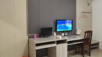 A room with a desk, a television, a chair, and a wall-mounted air conditioner.