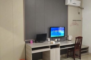 Una habitación con escritorio, televisor, silla y aire acondicionado instalado en la pared.