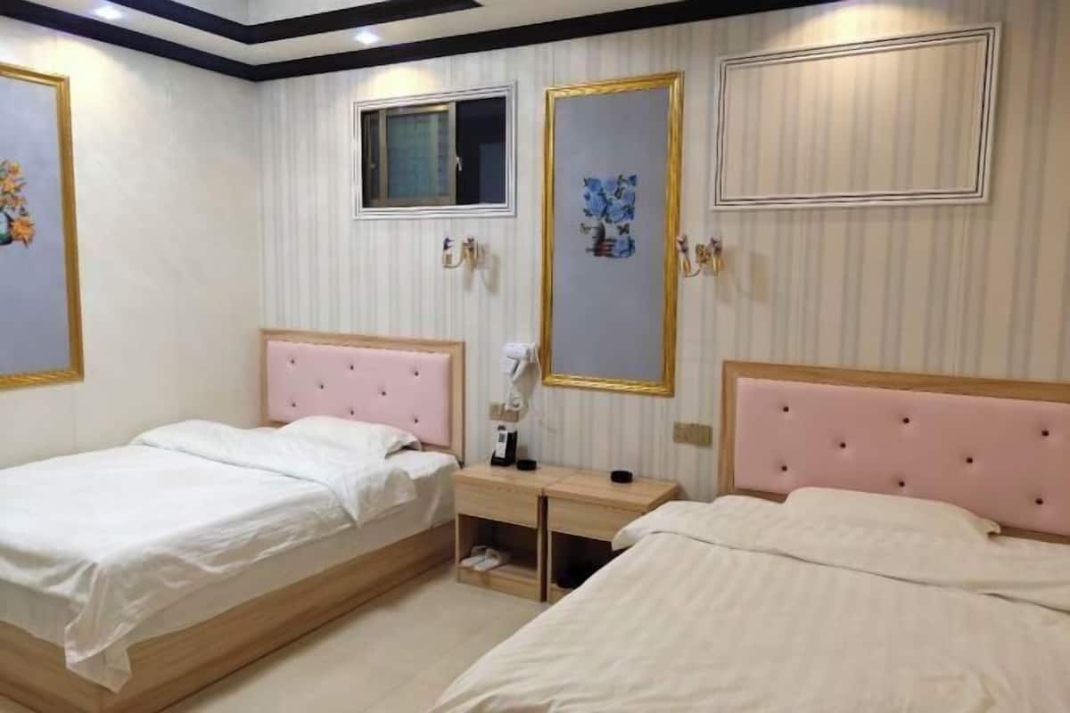 A hotel room with two beds, a small desk, a window, and decorative wall art.