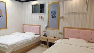 A hotel room with two beds, a small desk, a window, and decorative wall art.