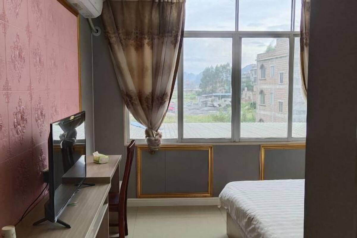 A room with a bed, a desk, a chair, a TV, and a window with curtains.
