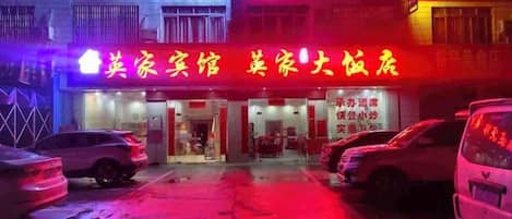 A building with a neon sign indicating a hotel and a restaurant. There are parked cars in front.