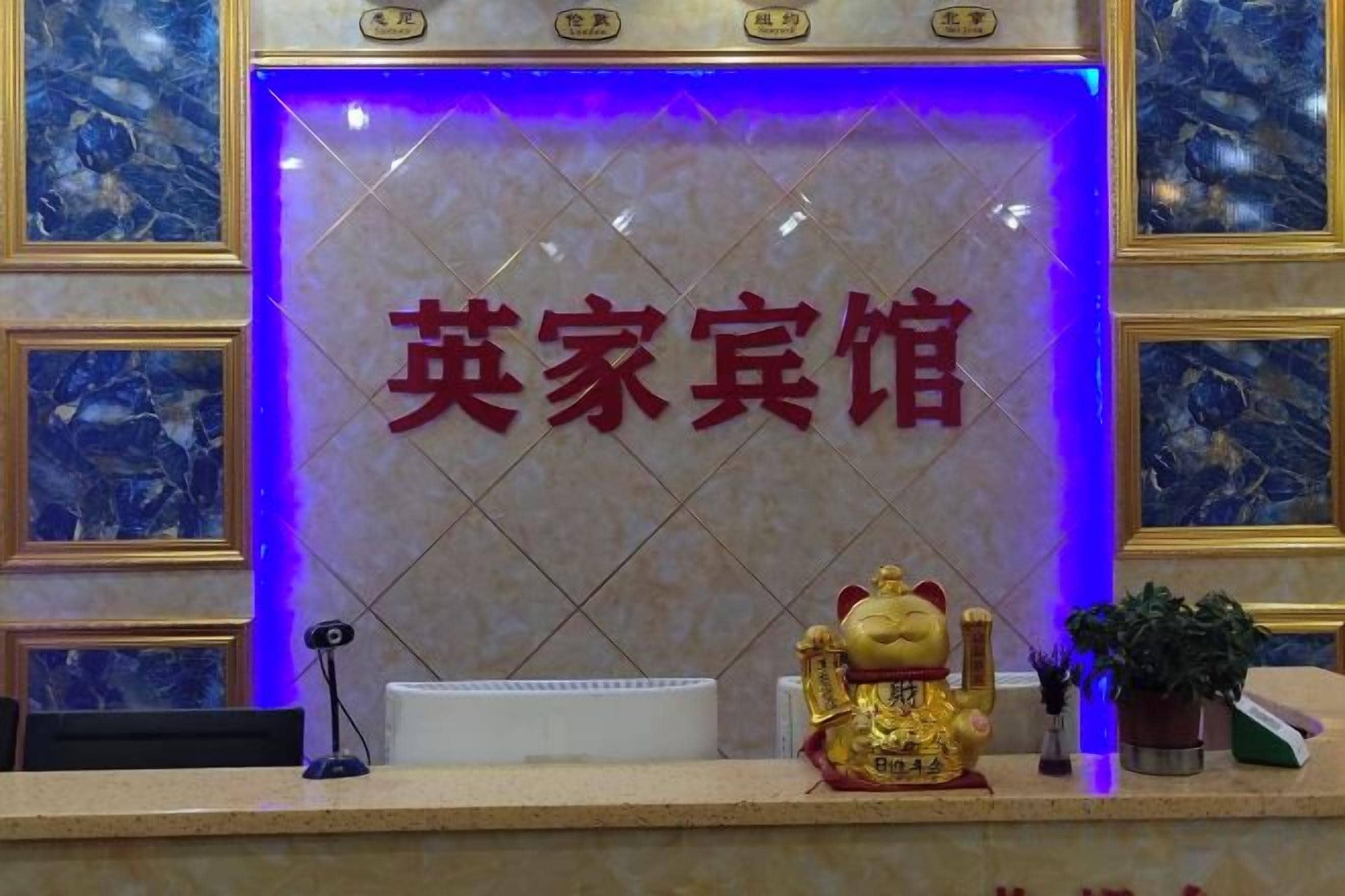 A reception desk with a sign that reads 'English Guest House' in red characters, a golden statue, and a potted plant.